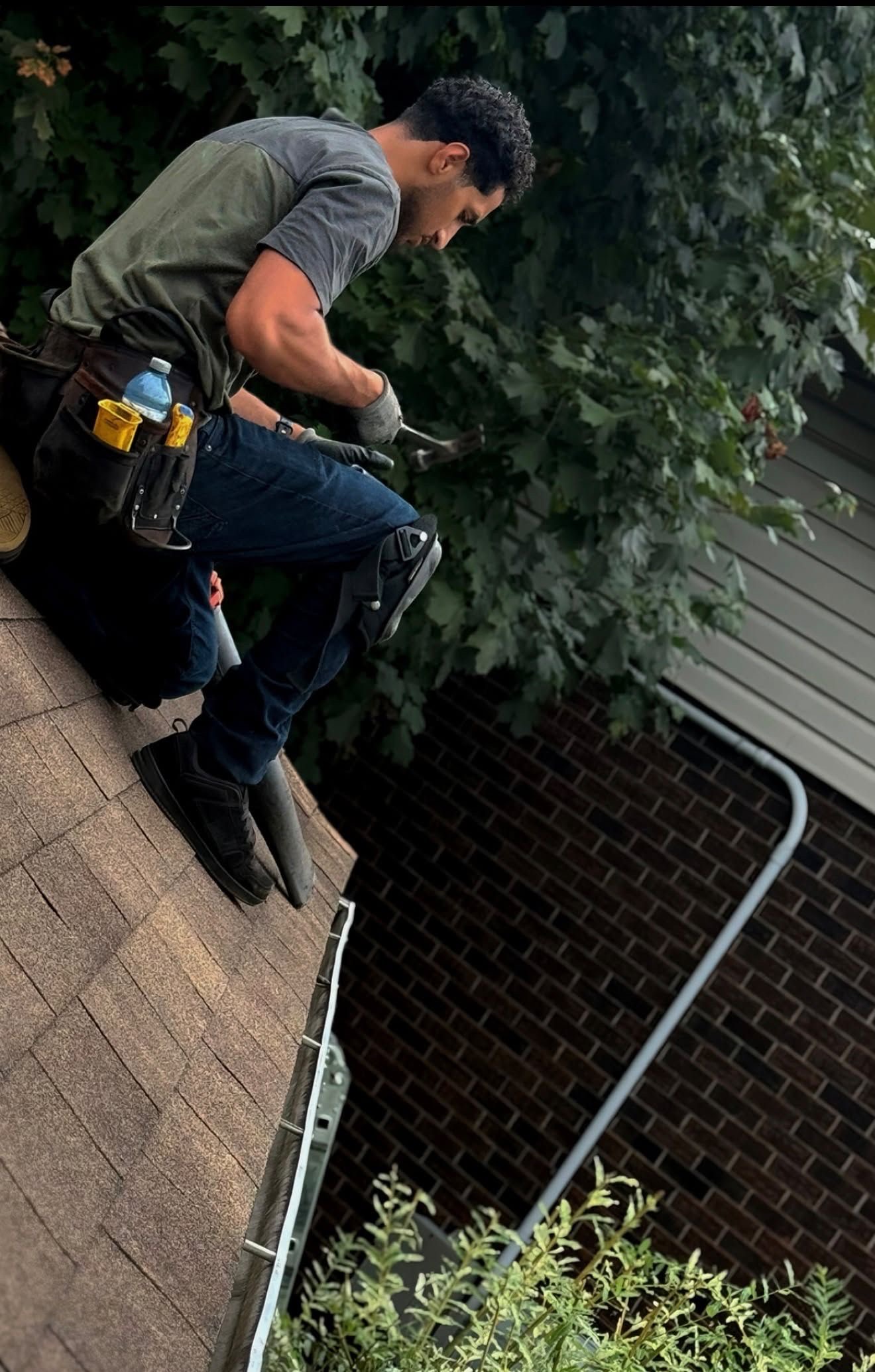 A roofer using hand tools while working on a shingled roof